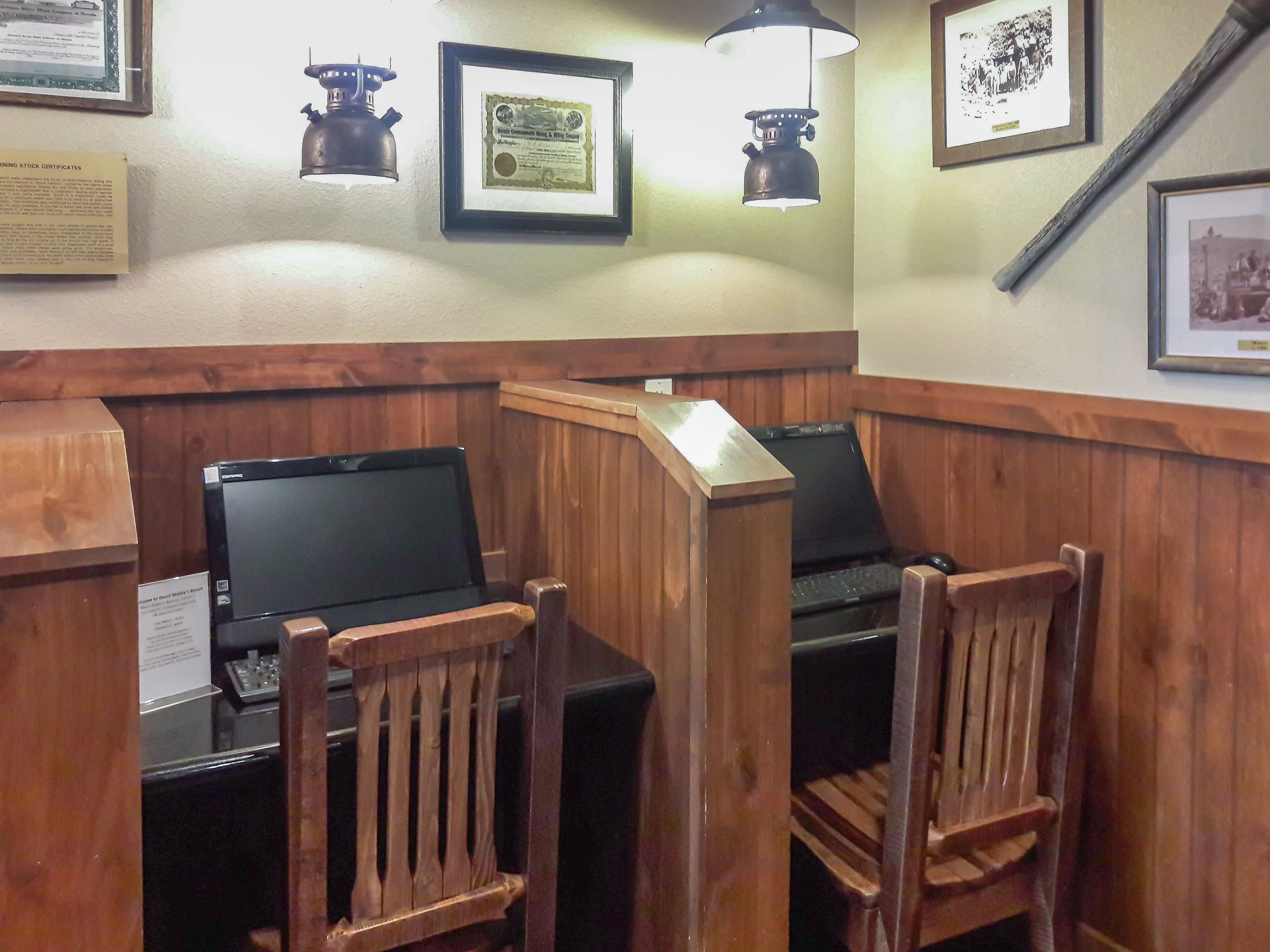 A corner room with two wooden desks, two chairs, a framed certificate, and a framed photograph on the wall.