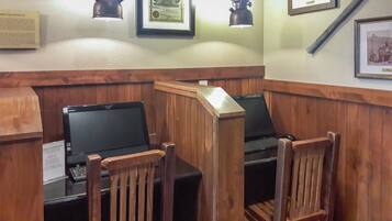 A corner room with two wooden desks, two chairs, a framed certificate, and a framed photograph on the wall.