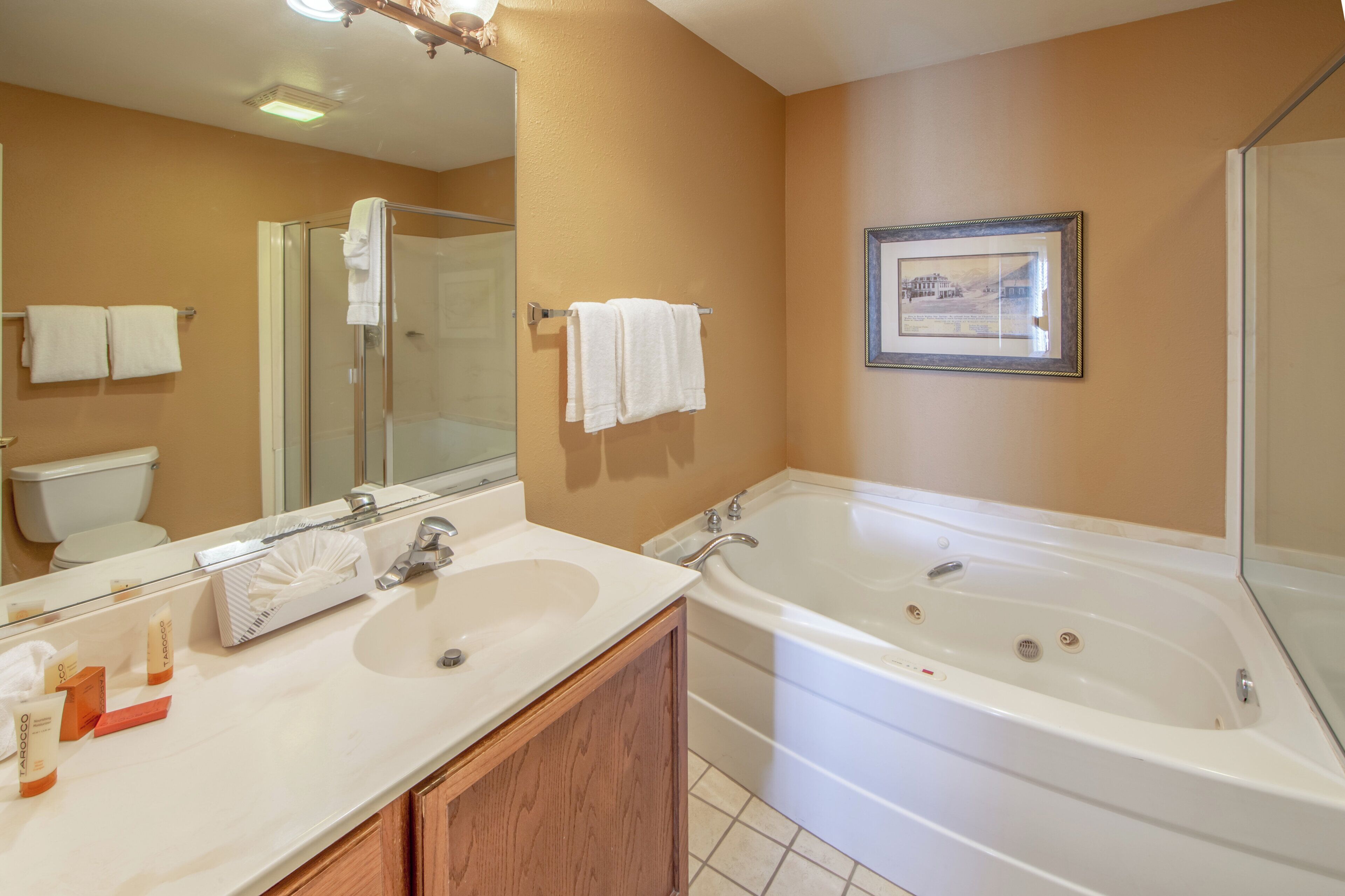 A bathroom with a large mirror, two sinks, a bathtub, and a shower.