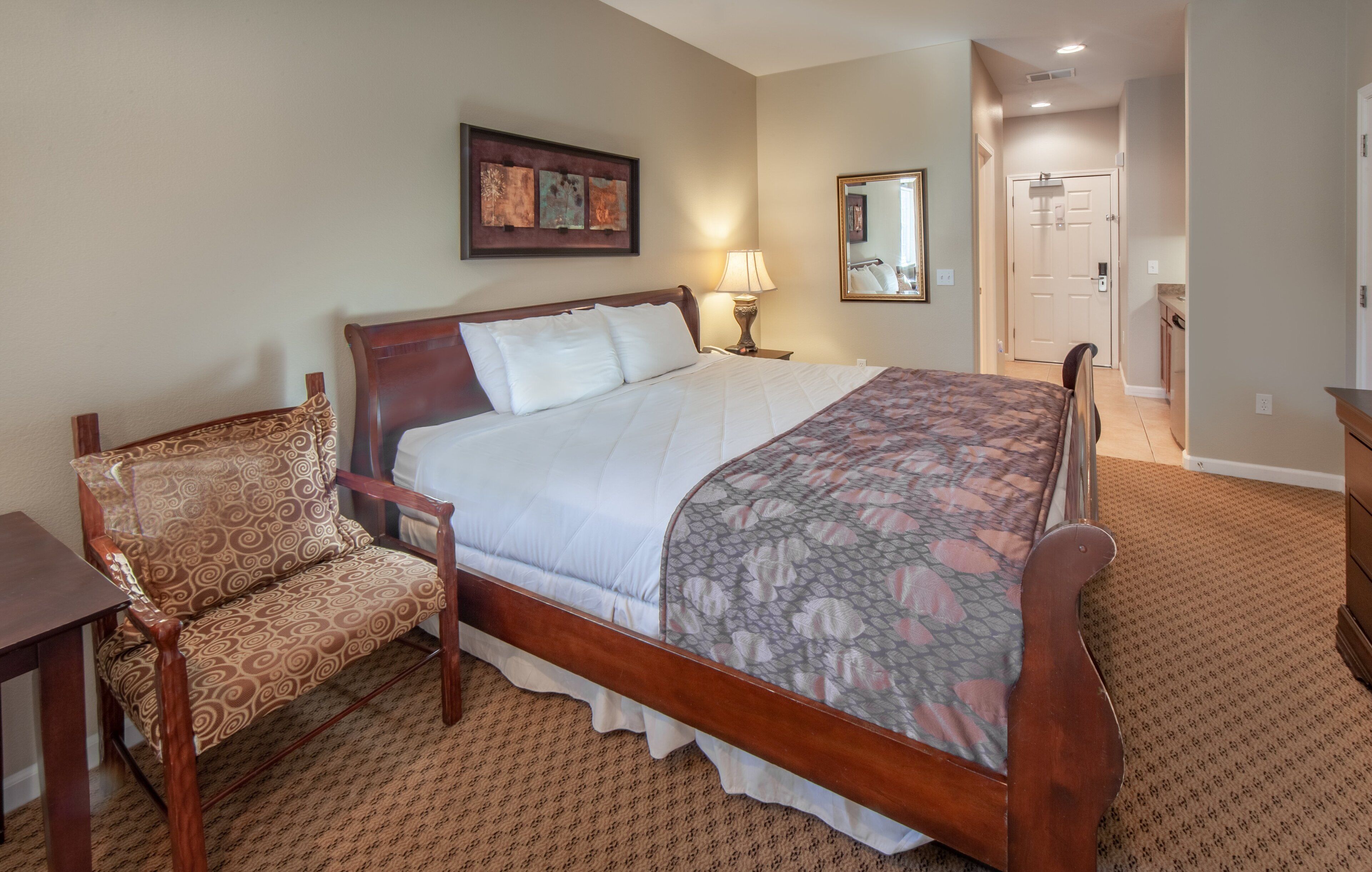 A bedroom with a wooden bed, a chair, a nightstand, a lamp, and a mirror.