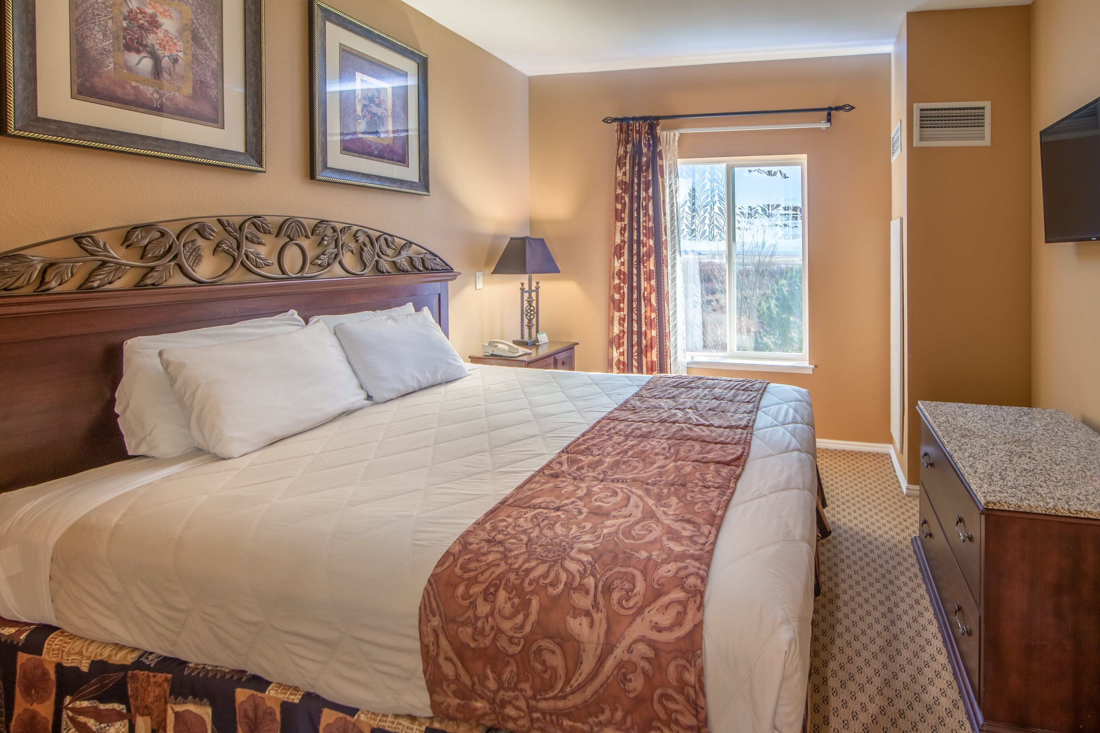 Une chambre d’hôtel avec un grand lit, une table de chevet, une commode et une fenêtre avec des rideaux.