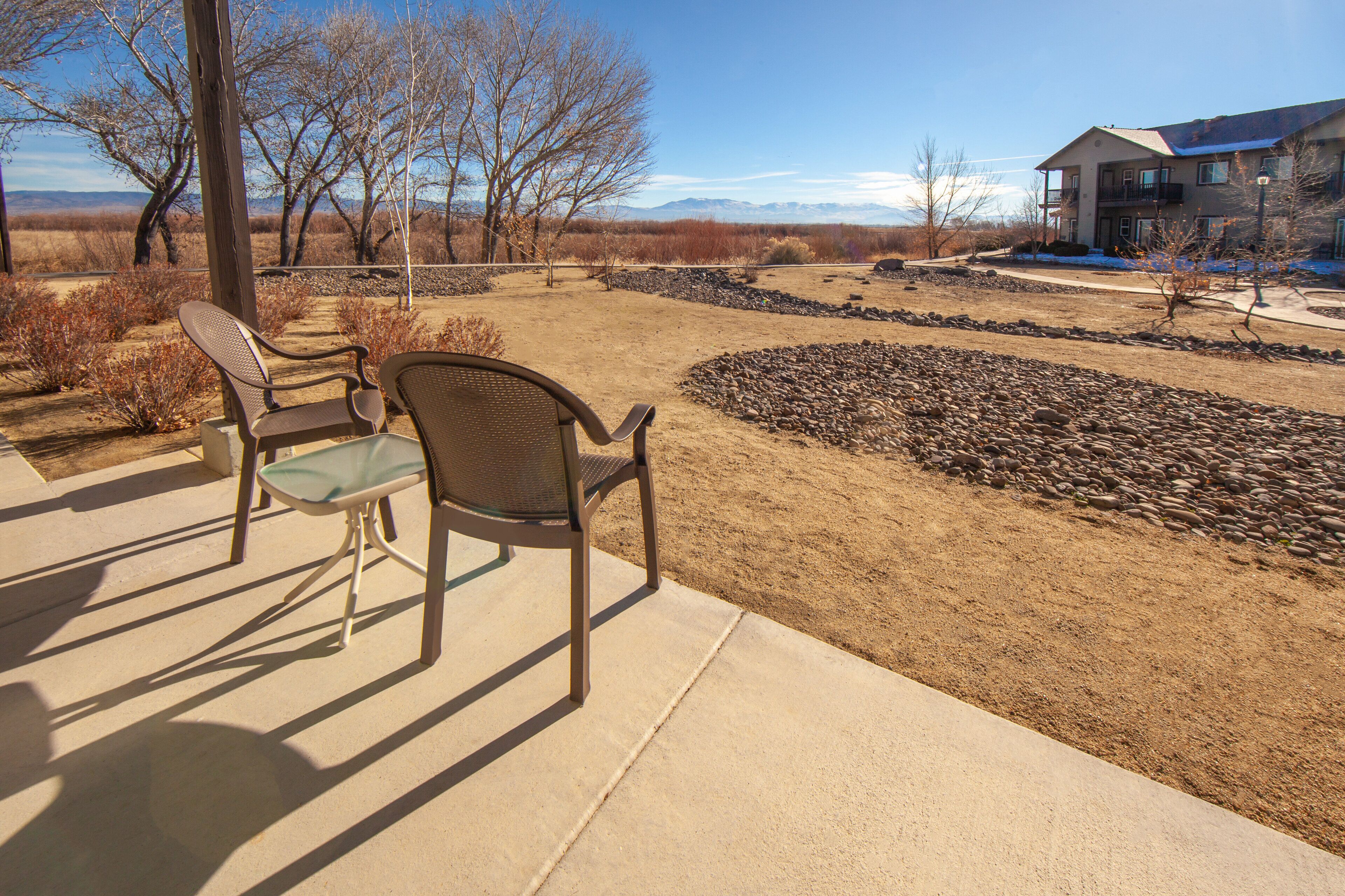A patio area with two chairs and a table, a stone pathway, and a building in the background.