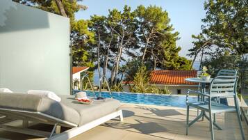 Ein Poolbereich mit Liegestuhl, Tisch und Stühlen sowie Blick auf das Meer und Bäume.