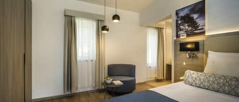 Una habitación de hotel moderna con una cama grande, una mesita redonda con un frutero, una silla y un cuadro en la pared.