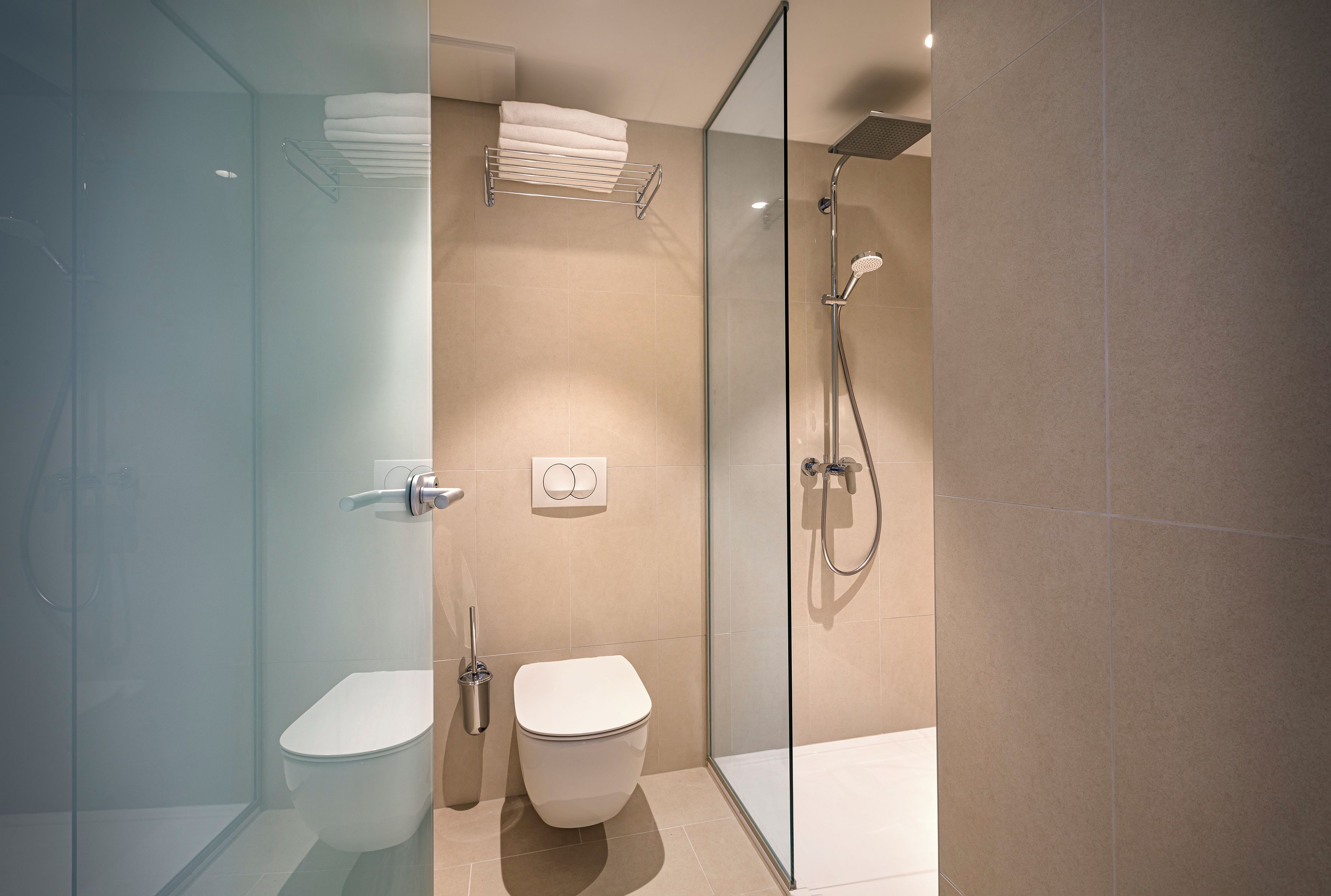 Een moderne badkamer met een glazen douchecabine, toilet en wastafel.