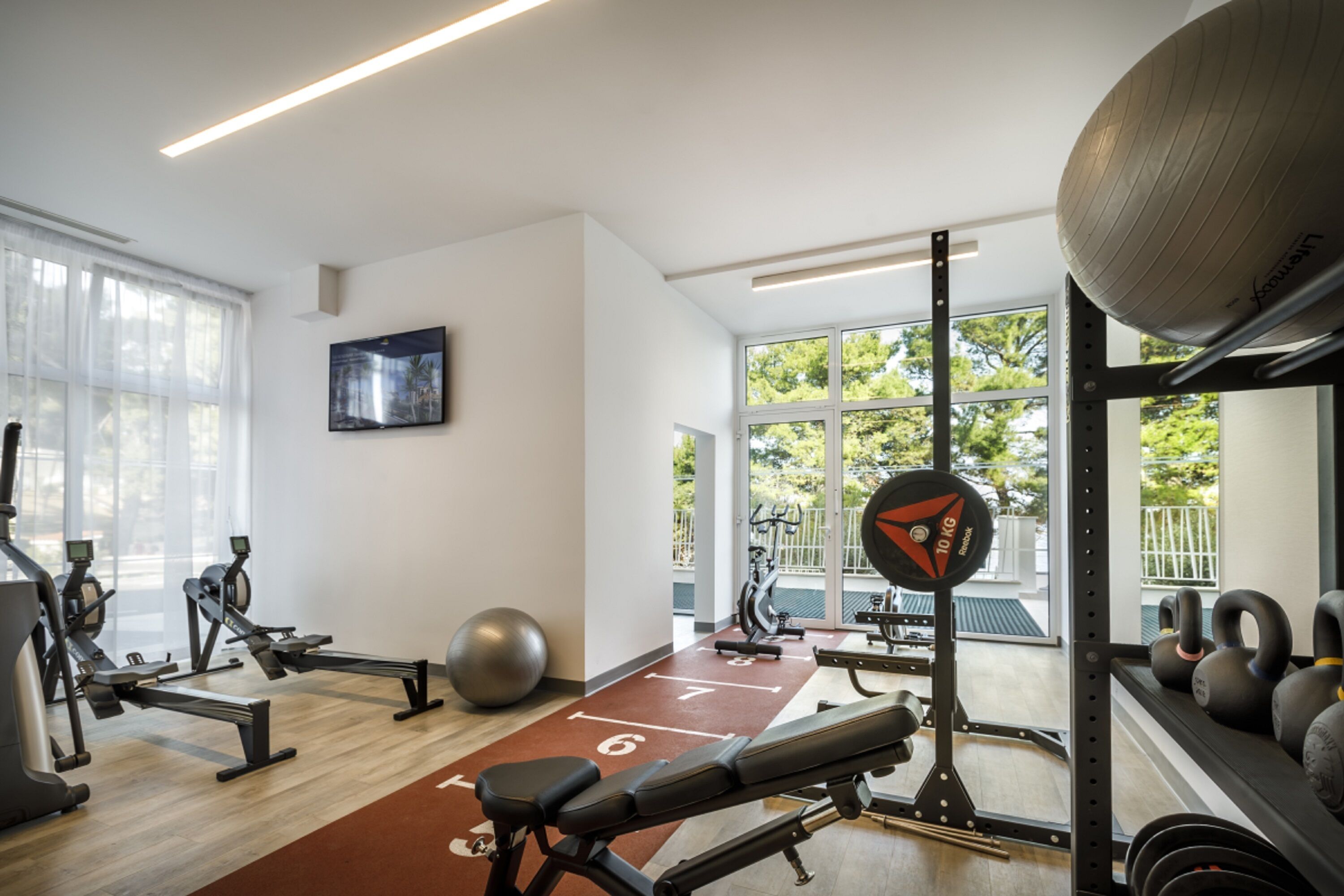 A gym with exercise equipment, a weight bench, and a large window with a view of trees.