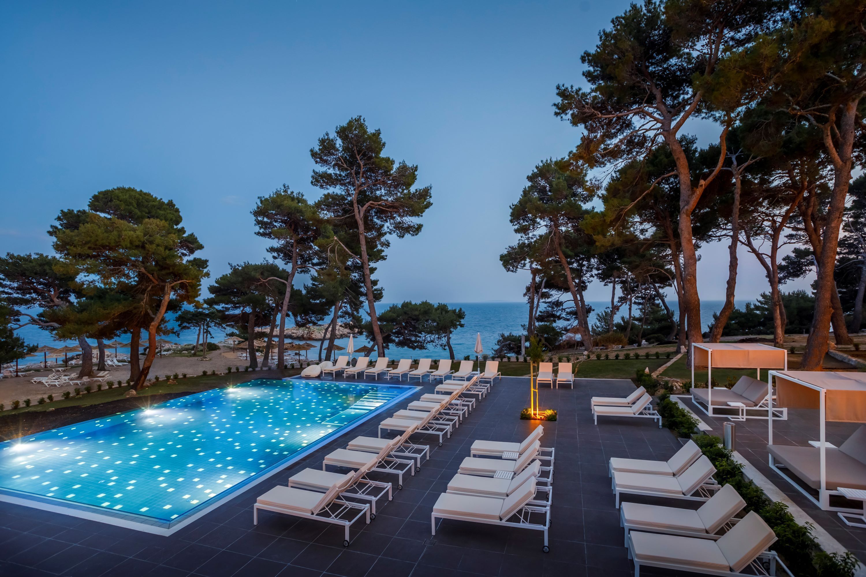 A poolside area with lounge chairs and a swimming pool, surrounded by trees and overlooking the sea.