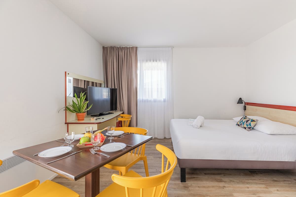 Een hotelkamer met een bed, een televisie, een eettafel met stoelen en een klein balkon.