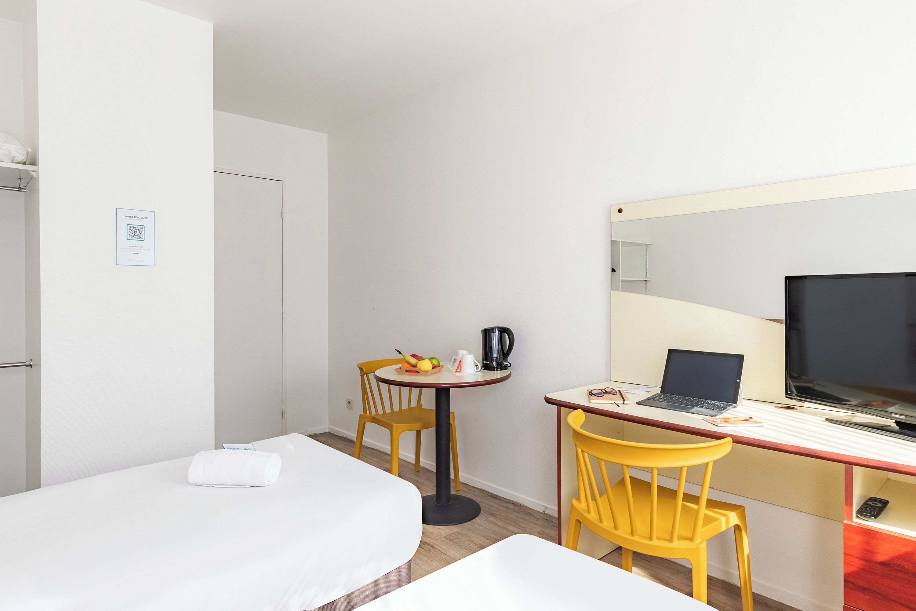 Une chambre d’hôtel avec un lit, un bureau avec un ordinateur portable, une télévision et une chaise.