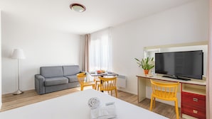 Een hotelkamer met een bed, een televisie, een bureau met een computer, een bank, een eettafel met stoelen en een potplant.