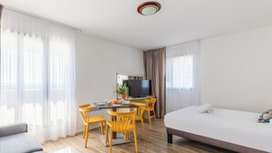 Een hotelkamer met een bed, een bureau met een televisie, een eettafel met stoelen en een bank.