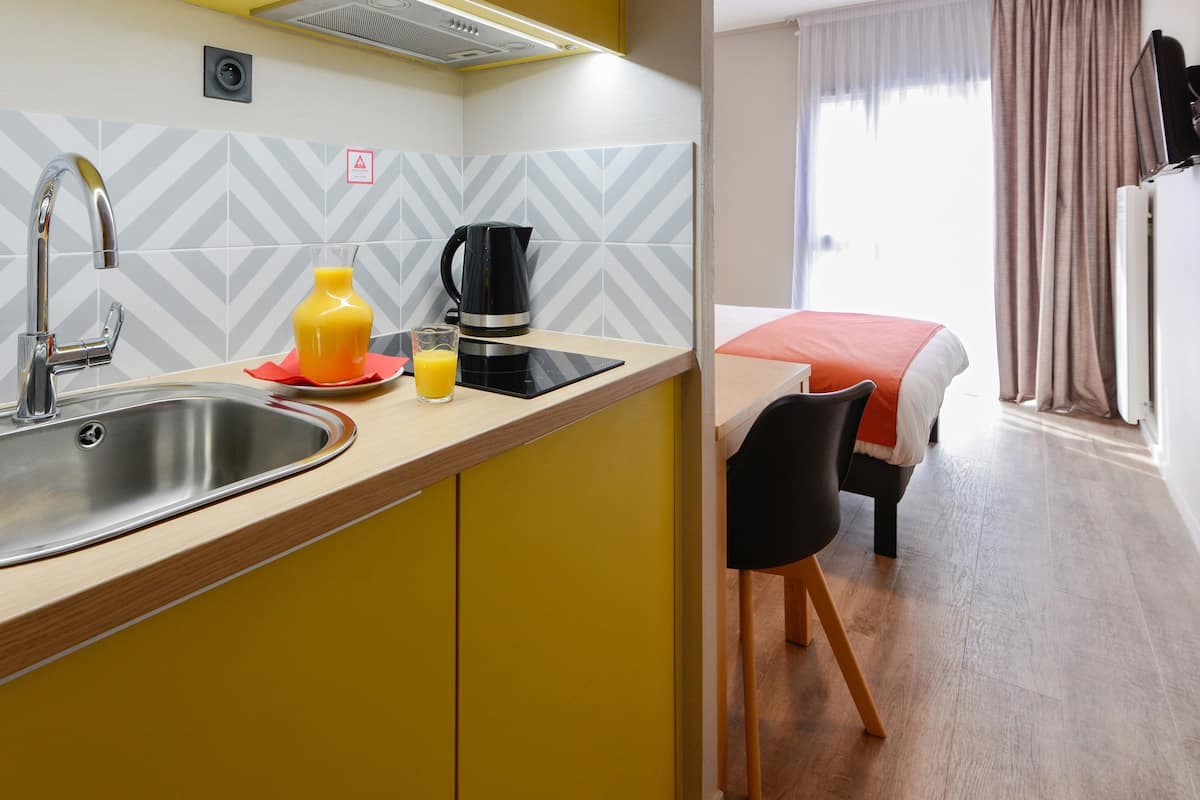 Een moderne kitchenette met een roestvrijstalen spoelbak, een koffiezetapparaat en een glas sinaasappelsap op het aanrecht.