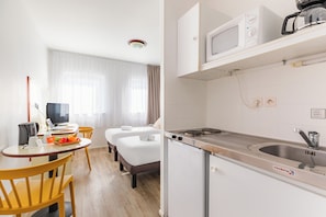 Une chambre d’hôtel comprenant un lit, un bureau avec un ordinateur, et un petit coin cuisine équipé d’un four à micro-ondes et d’un évier.