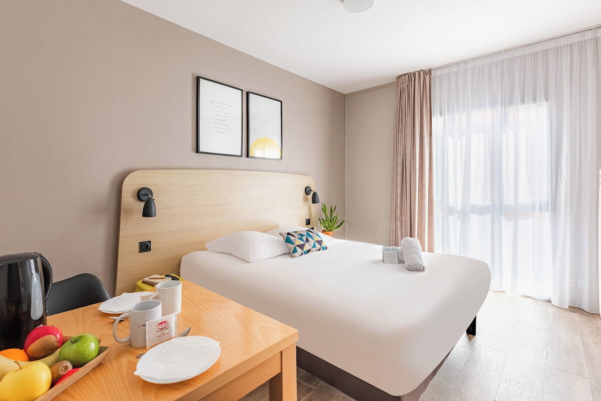 Een hotelkamer met een bed, een houten tafel met fruit, een waterkoker en een koffiezetapparaat.