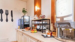 Een ontbijtbuffet met een koffieapparaat, een schaal fruit en diverse ontbijtartikelen.