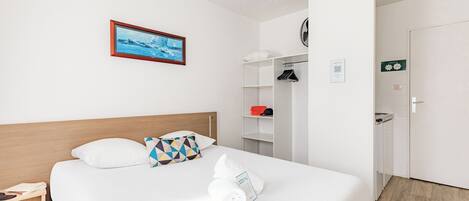 A hotel room with a neatly made bed, a wooden headboard, a framed picture on the wall, a wardrobe, and a door with a sign.