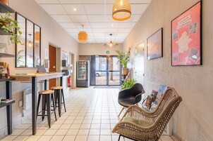 Un espace d’accueil comprenant un comptoir, des tabourets de bar, un fauteuil en osier avec des magazines et une grande affiche encadrée au mur.