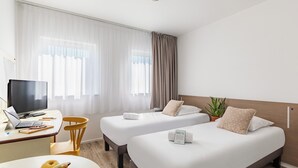 Een hotelkamer met twee bedden, een bureau met een laptop, een fruitschaal en een potplant.