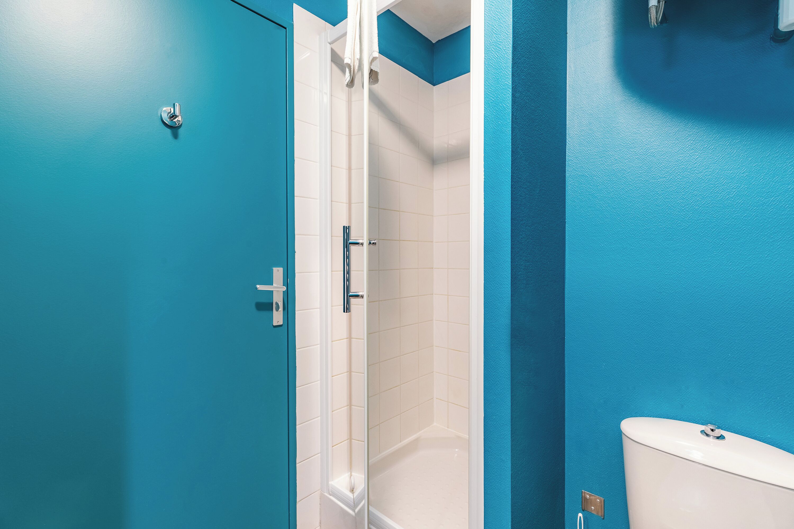A bathroom with a blue wall, a white toilet, and a shower stall.