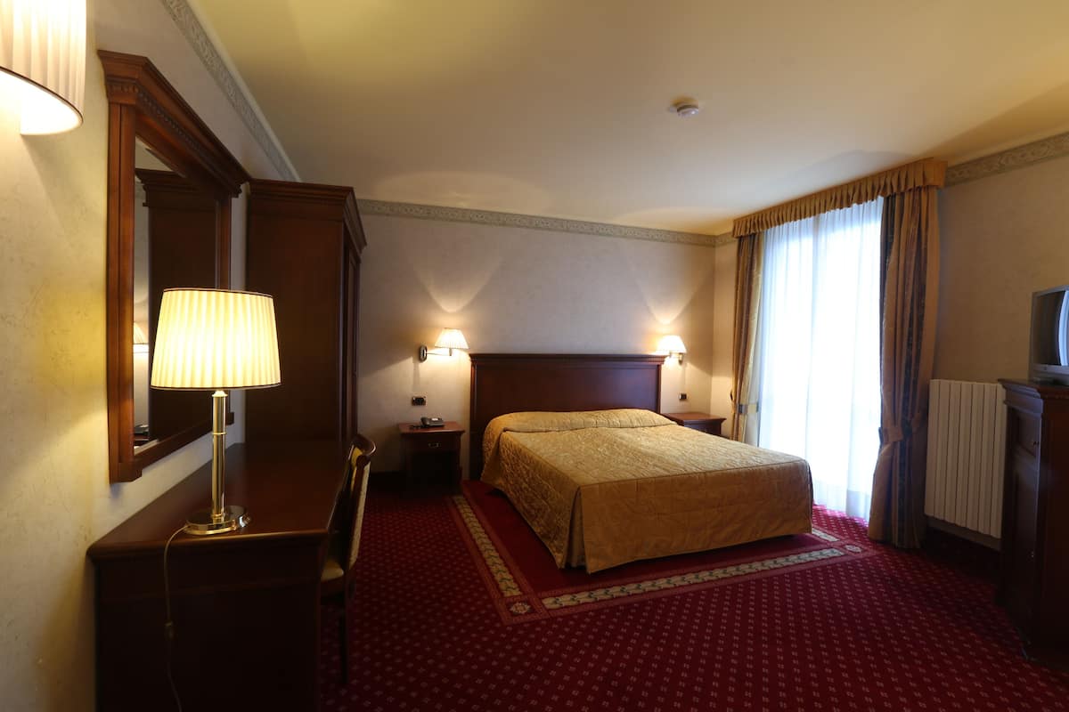 Una habitación de hotel con cama, escritorio, silla, lámpara y espejo.