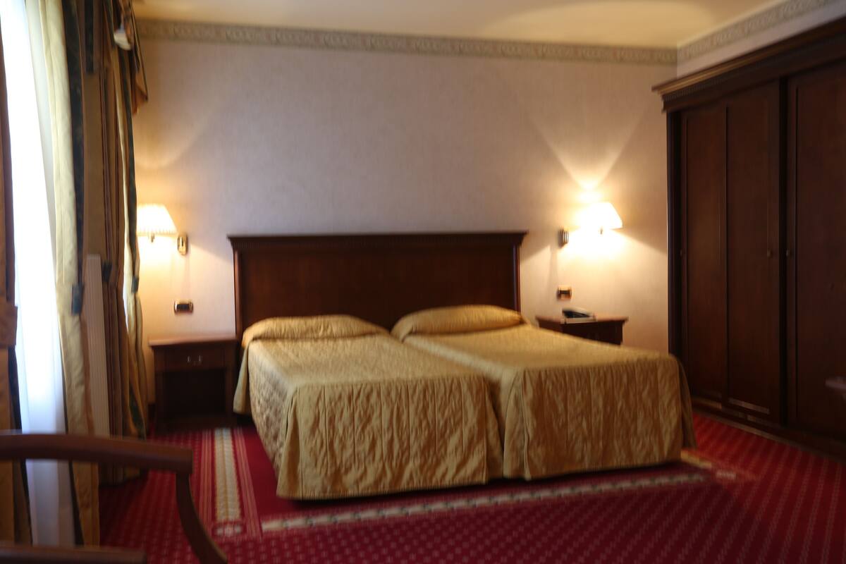 Habitación de hotel con cama doble, dos mesitas de noche, un armario y dos lámparas de pared.
