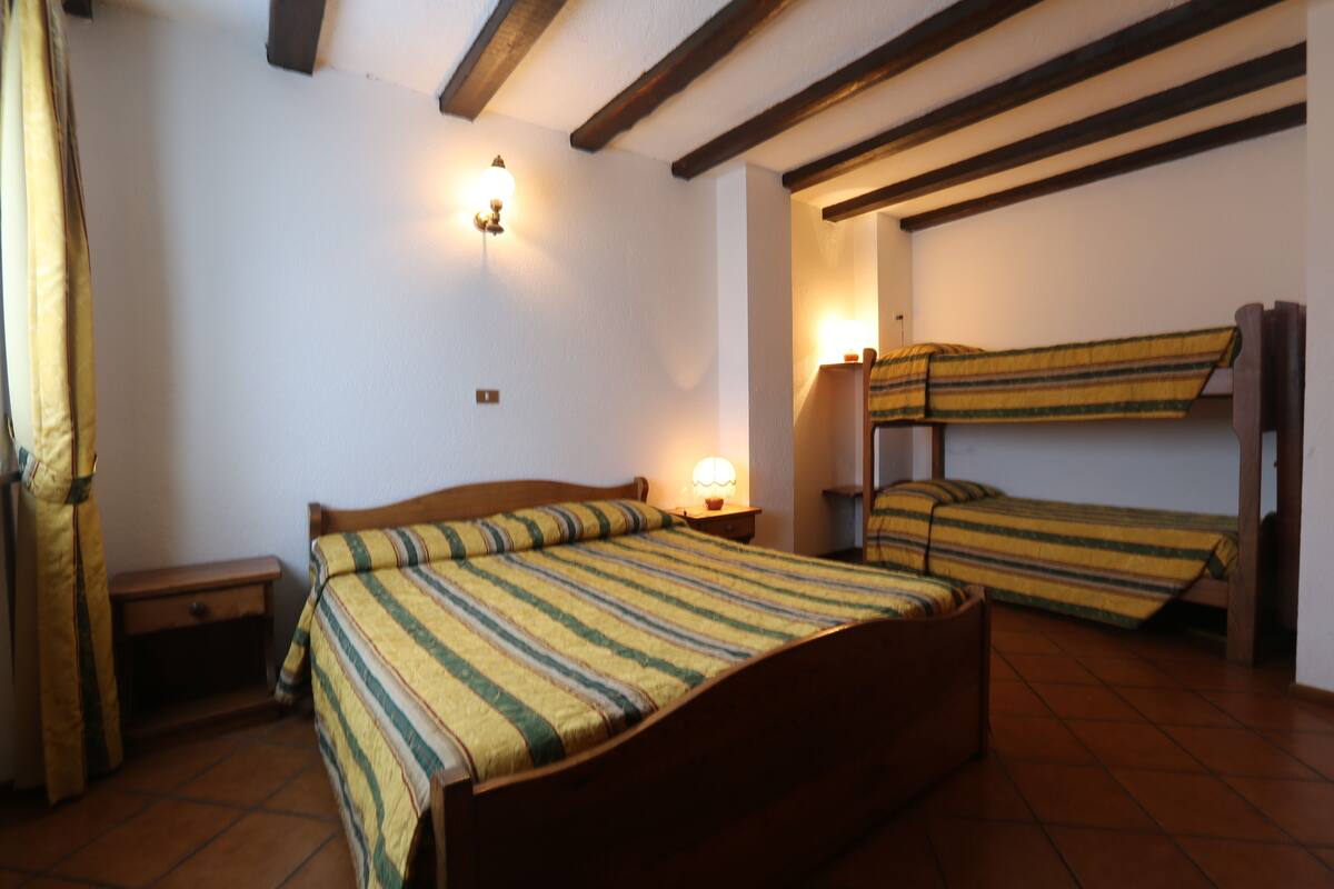 Una habitación con una cama individual, una mesita de noche, una lámpara y una cama litera.