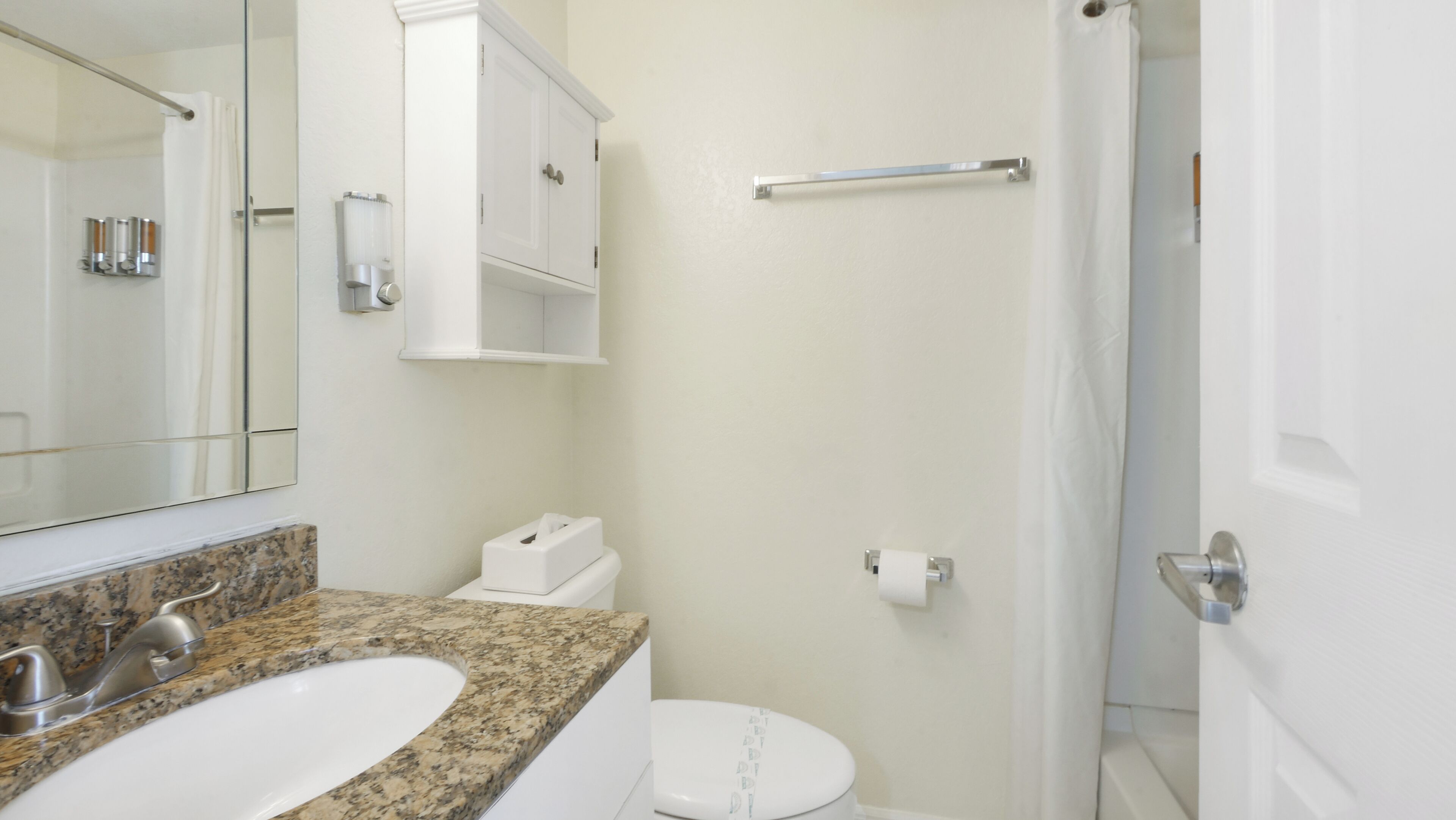 Un baño con encimera de granito, lavamanos blanco, inodoro y zona de ducha.
