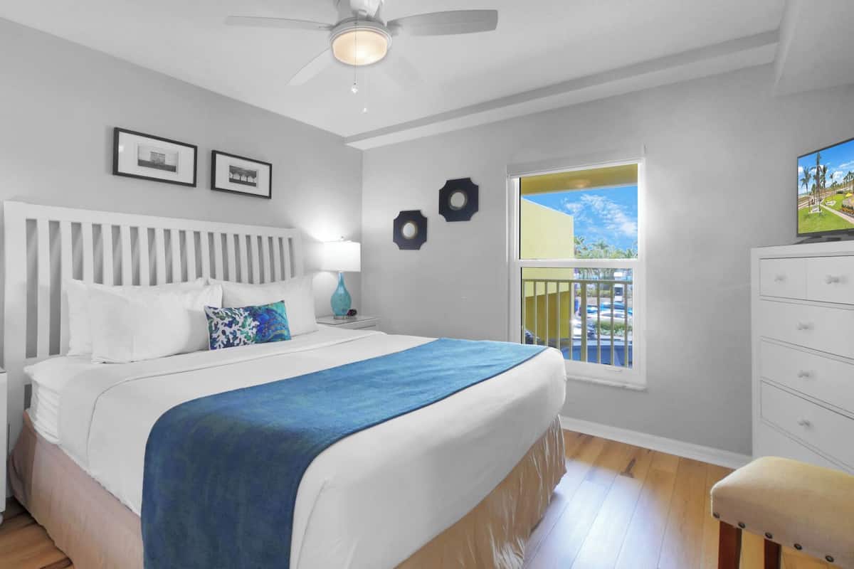 A bedroom with a bed, nightstands, a dresser, a window with a view, and a ceiling fan.