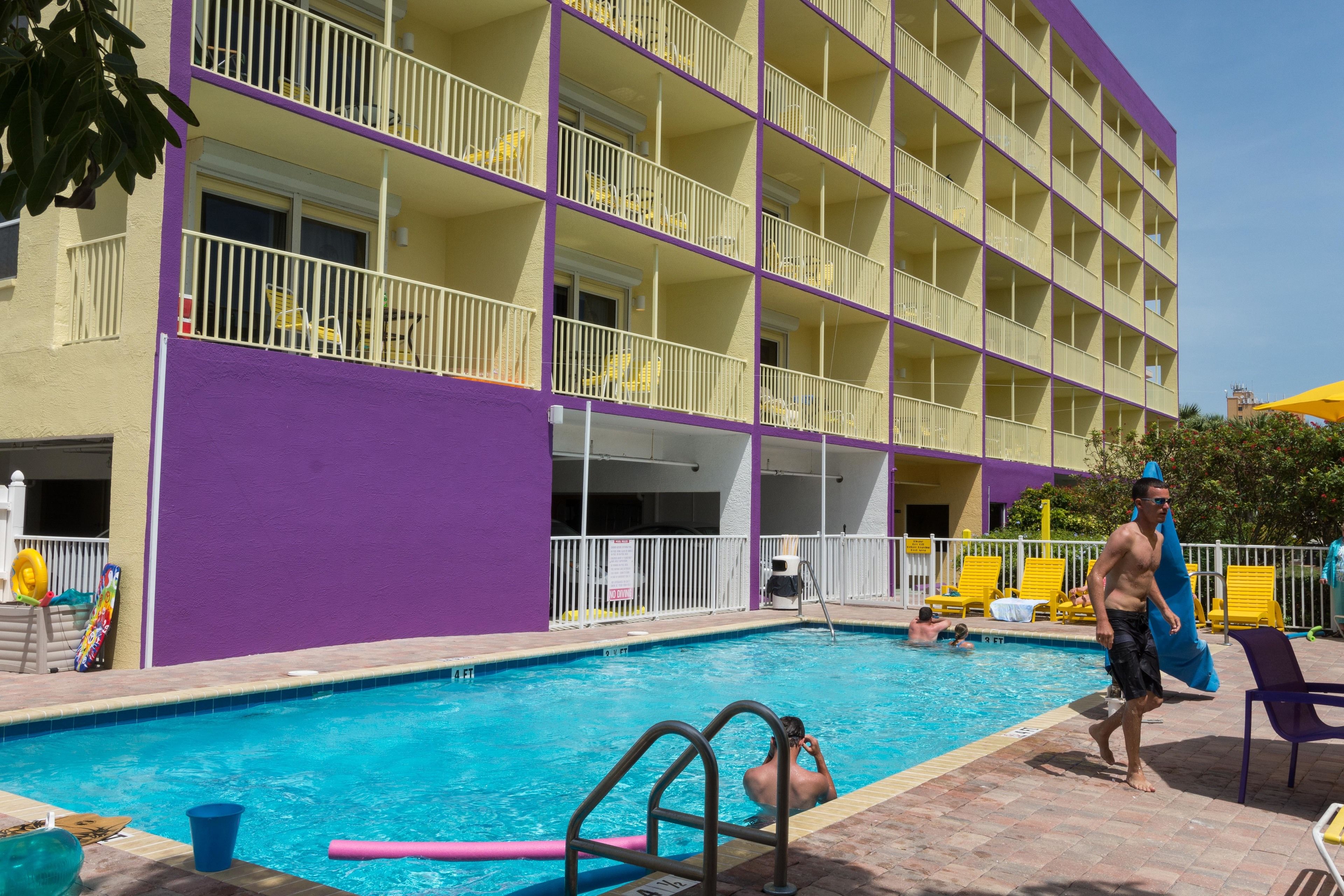 A hotel with a swimming pool, multiple balconies, and sun loungers.