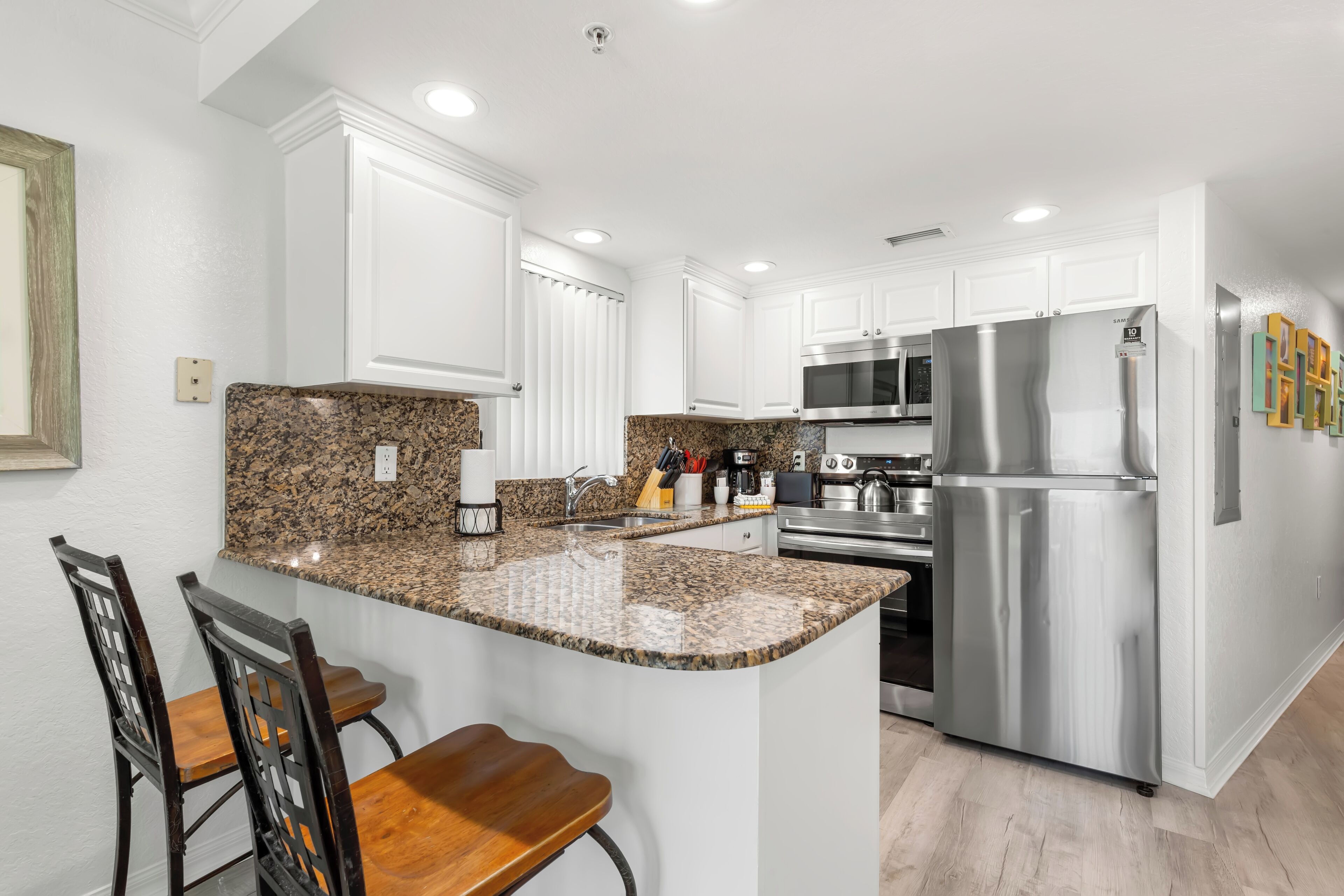A modern kitchen with white cabinetry, granite countertops, stainless steel appliances, and a bar area with wooden chairs.