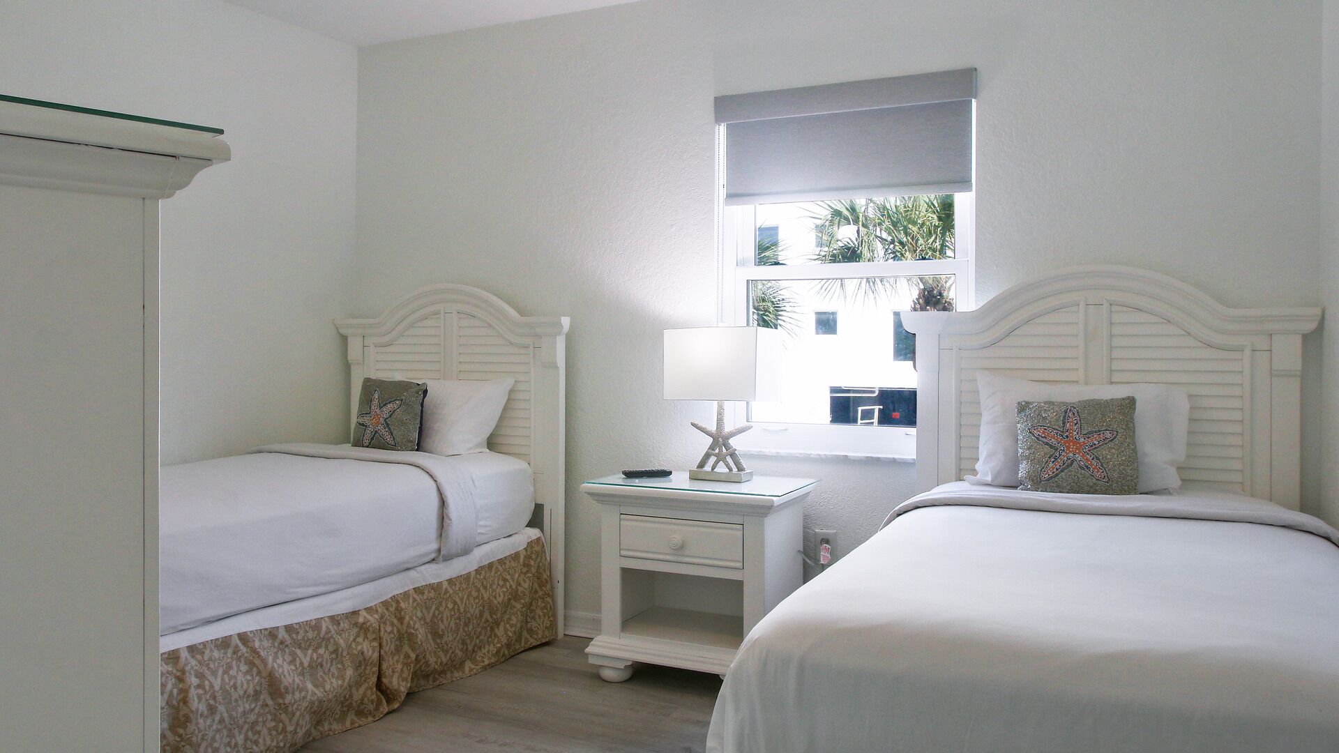 A twin bedroom with two beds, a nightstand, and a window with a view.
