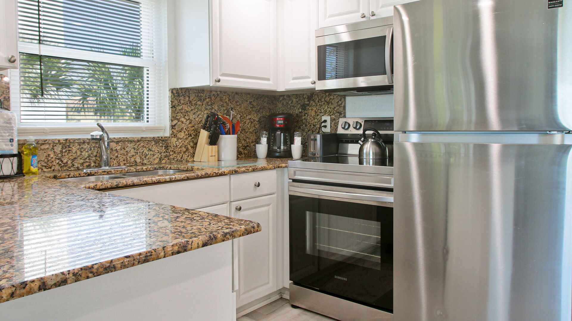 A modern kitchen with granite countertops, stainless steel appliances, and white cabinetry.