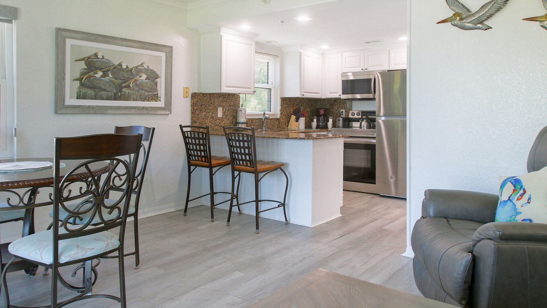 A modern kitchen with white cabinets, stainless steel appliances, and a granite countertop. There is a dining area with a table and chairs.