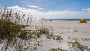 A beach with sand, sparse vegetation, and a tent.