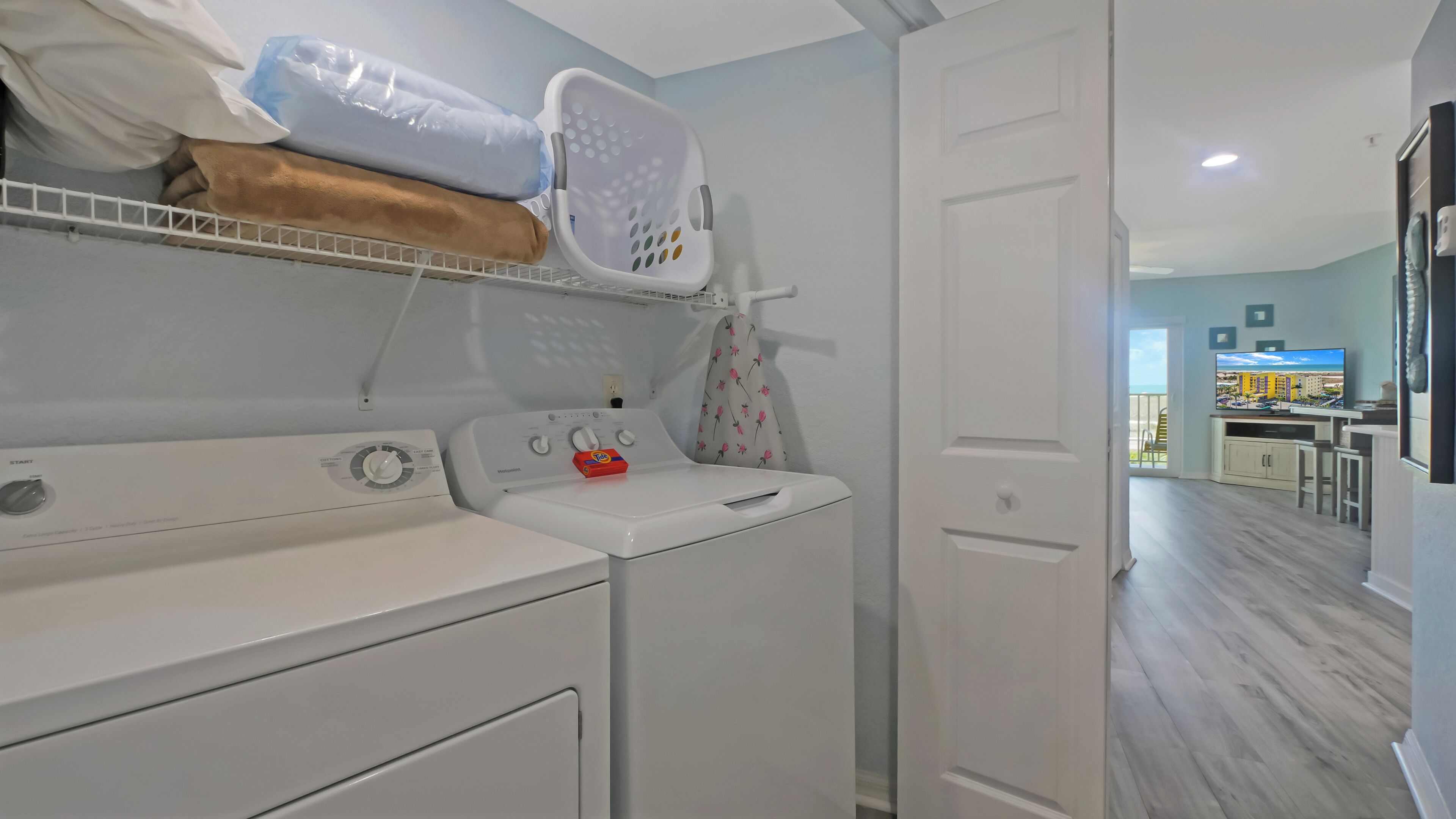 A laundry area with two washing machines, a drying rack, and a wall-mounted ironing board.