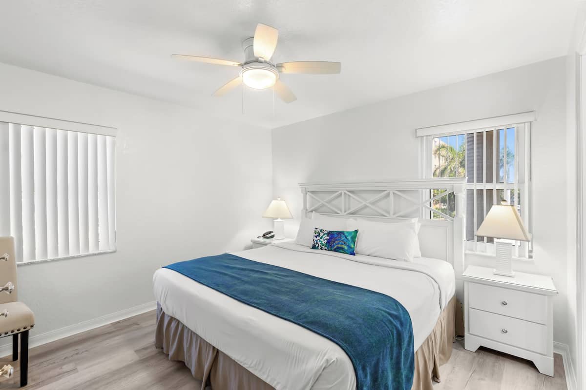 A bedroom with a bed, bedside tables, a ceiling fan, and a window with blinds.