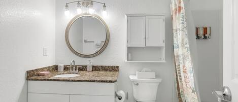 A bathroom with a sink, mirror, toilet, and shower curtain.