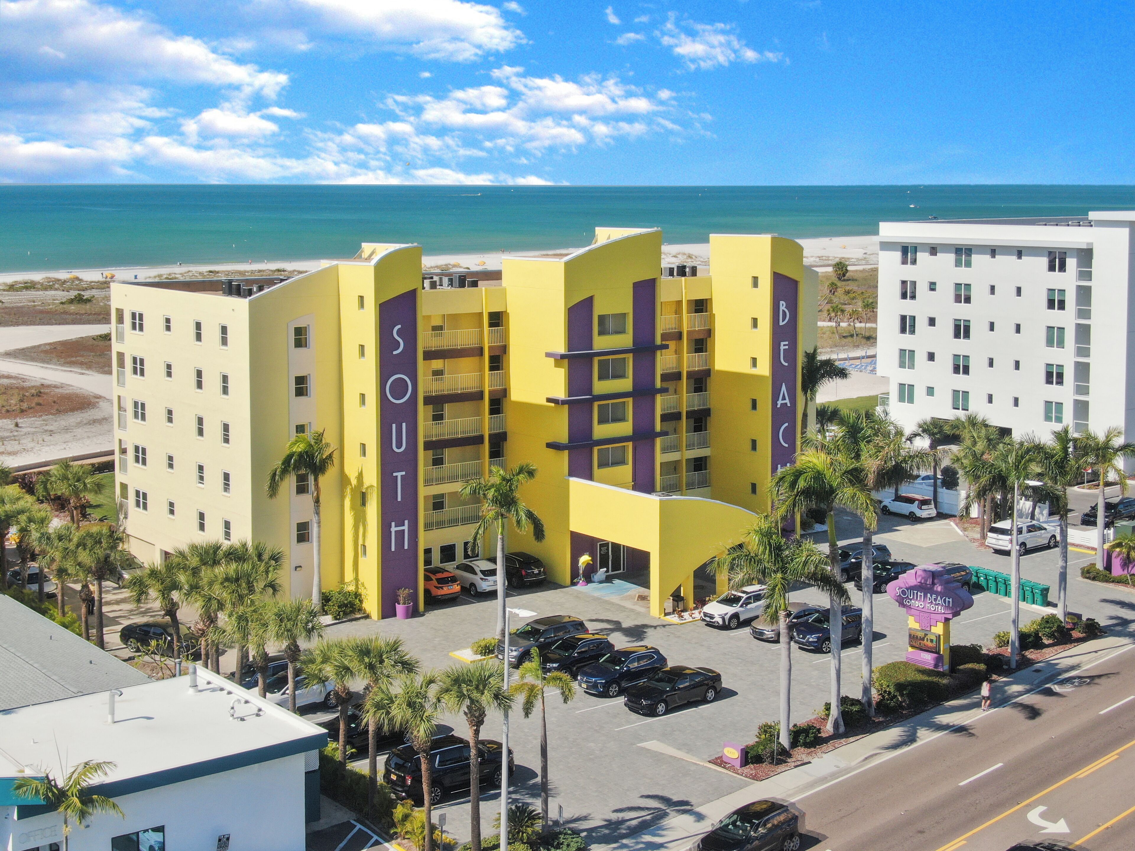 Un hotel de varios pisos con un cartel llamativo que dice 'SOUTH', zona de estacionamiento y vista a la playa.