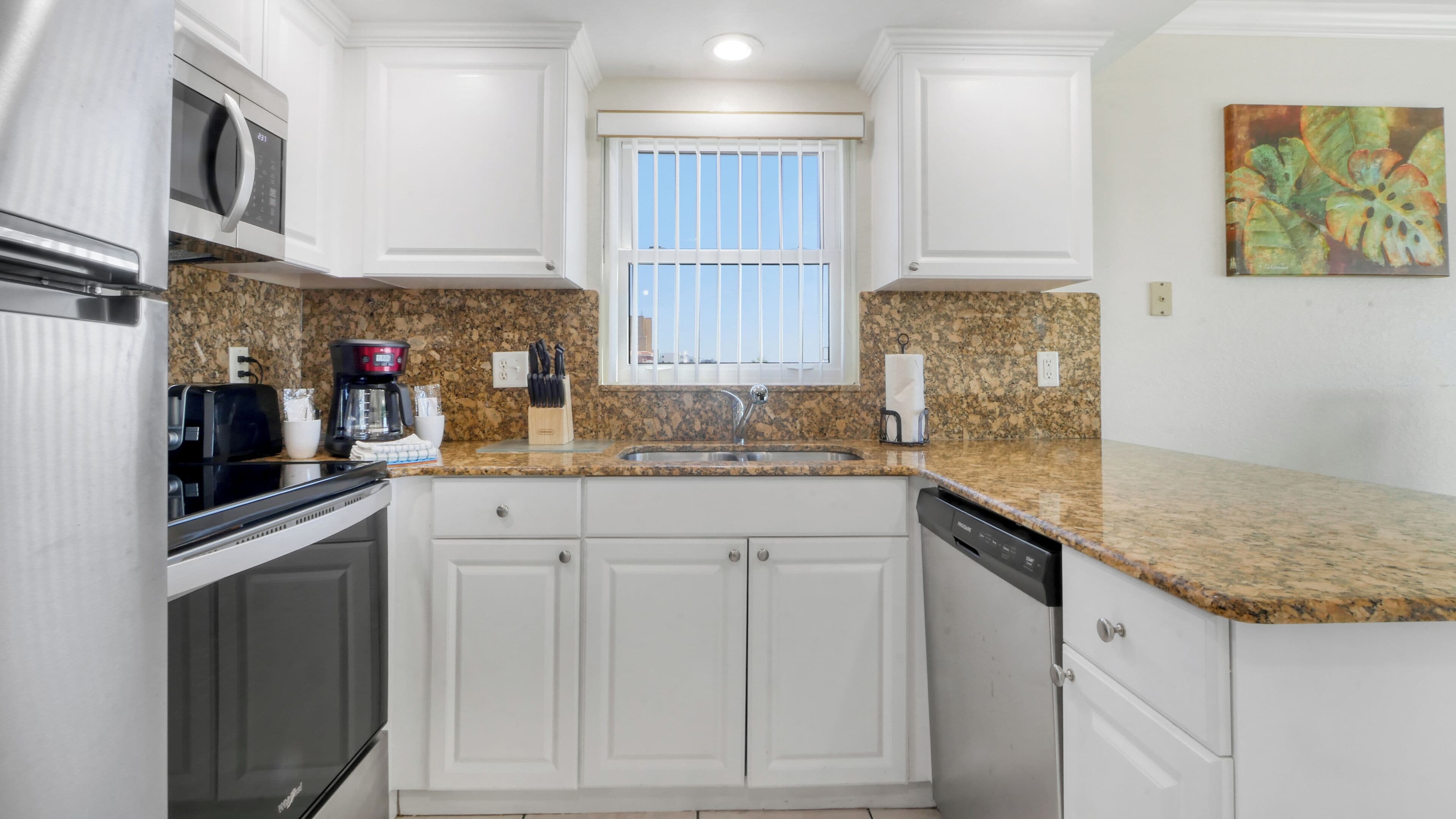 A kitchen with white cabinets, a granite countertop, a stainless steel sink, a coffee maker, and a microwave.