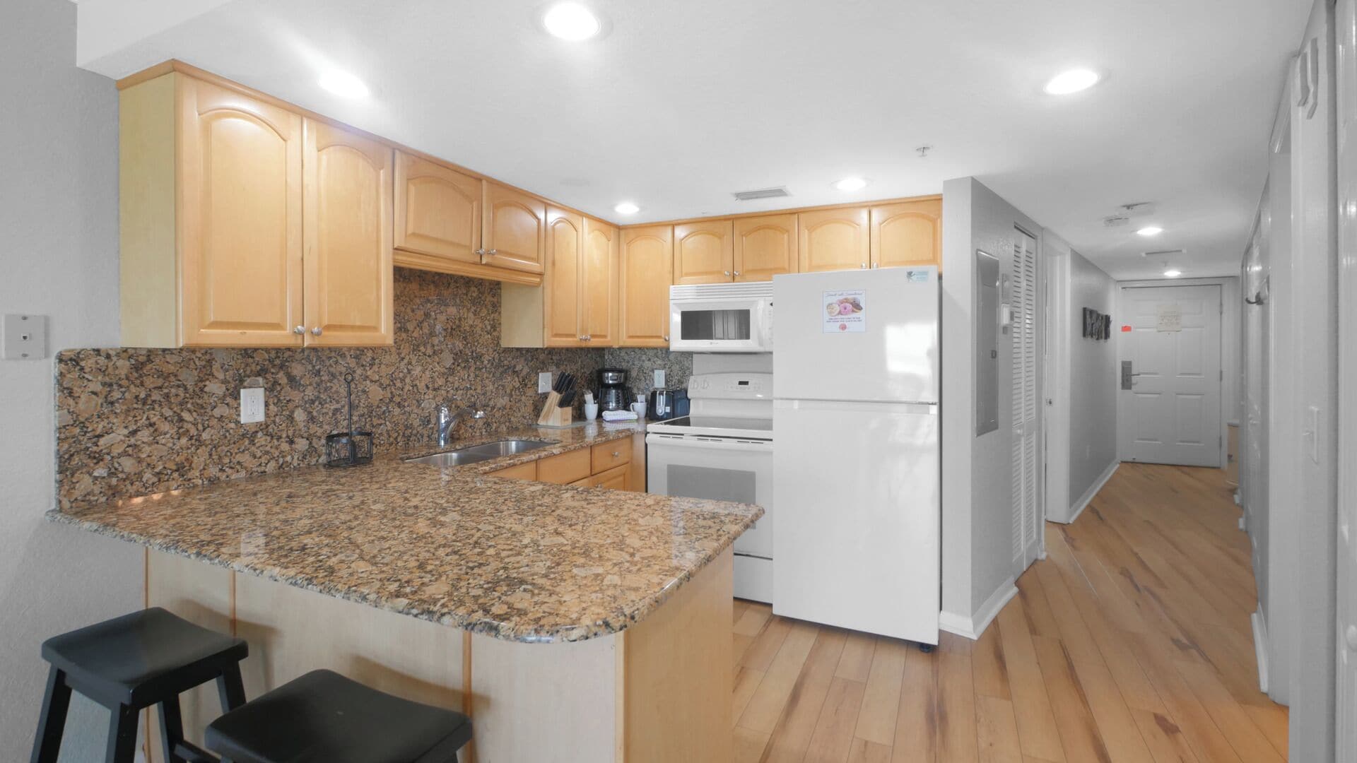 A modern kitchen with granite countertops, wooden cabinets, a built-in microwave, and a refrigerator.