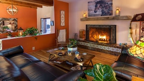 A cozy living room with a fireplace, leather sofas, wooden coffee table, and various decorative items. - Adobe Rose Inn B&B (Tucson)