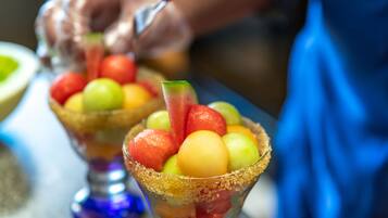 Primer plano de un plato de frutas con borde azucarado, una cuchara y una persona al fondo.