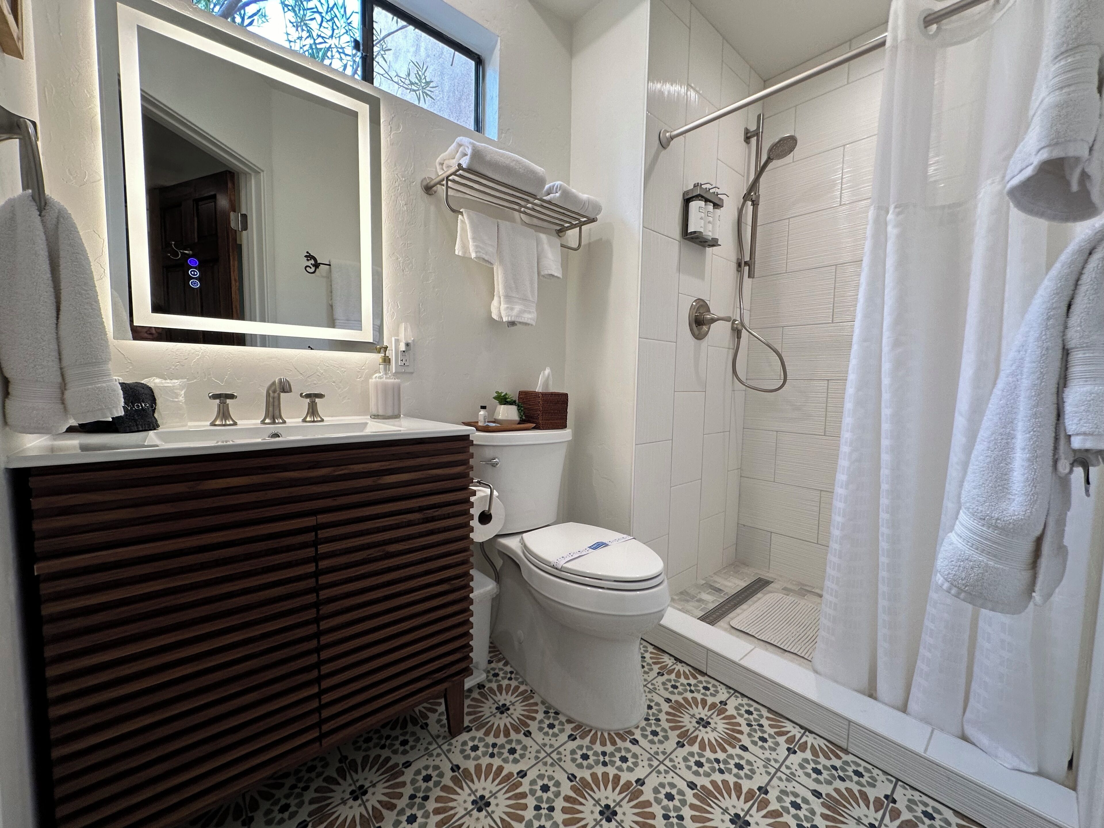 A modern bathroom with a wooden vanity, a toilet, a shower with a glass door, and a large mirror.