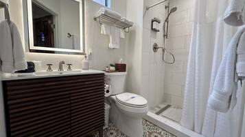 A modern bathroom with a wooden vanity, a toilet, a shower with a glass door, and a large mirror.