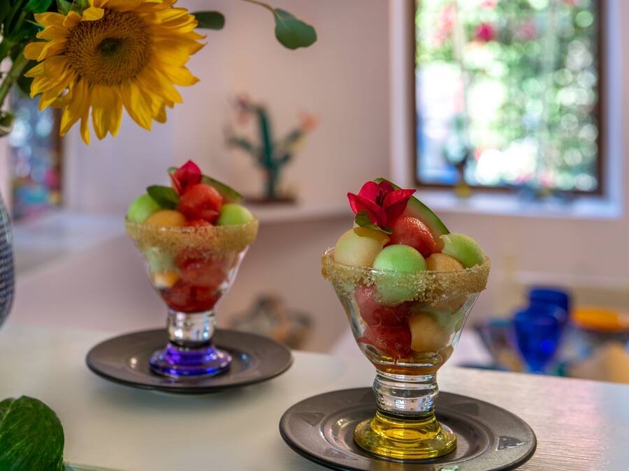Two dessert glasses on a table with a vase of sunflowers and a decorative cactus in the background.