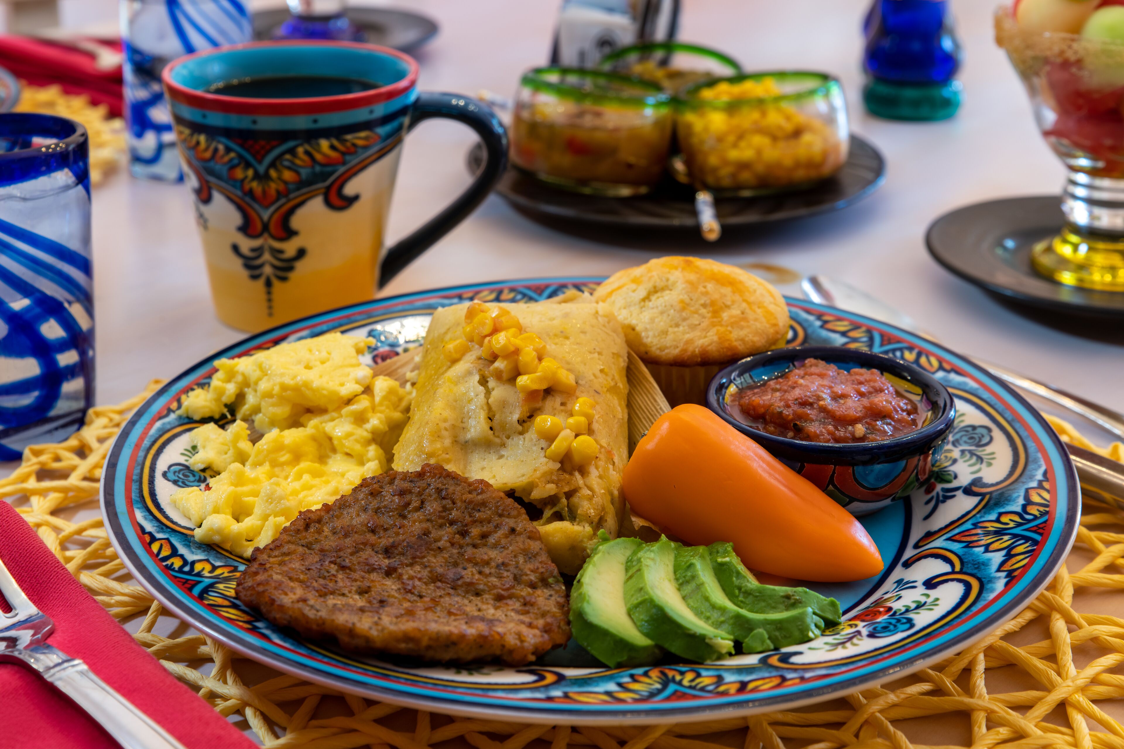 A plate with scrambled eggs, sausage, avocado, and a baked potato.