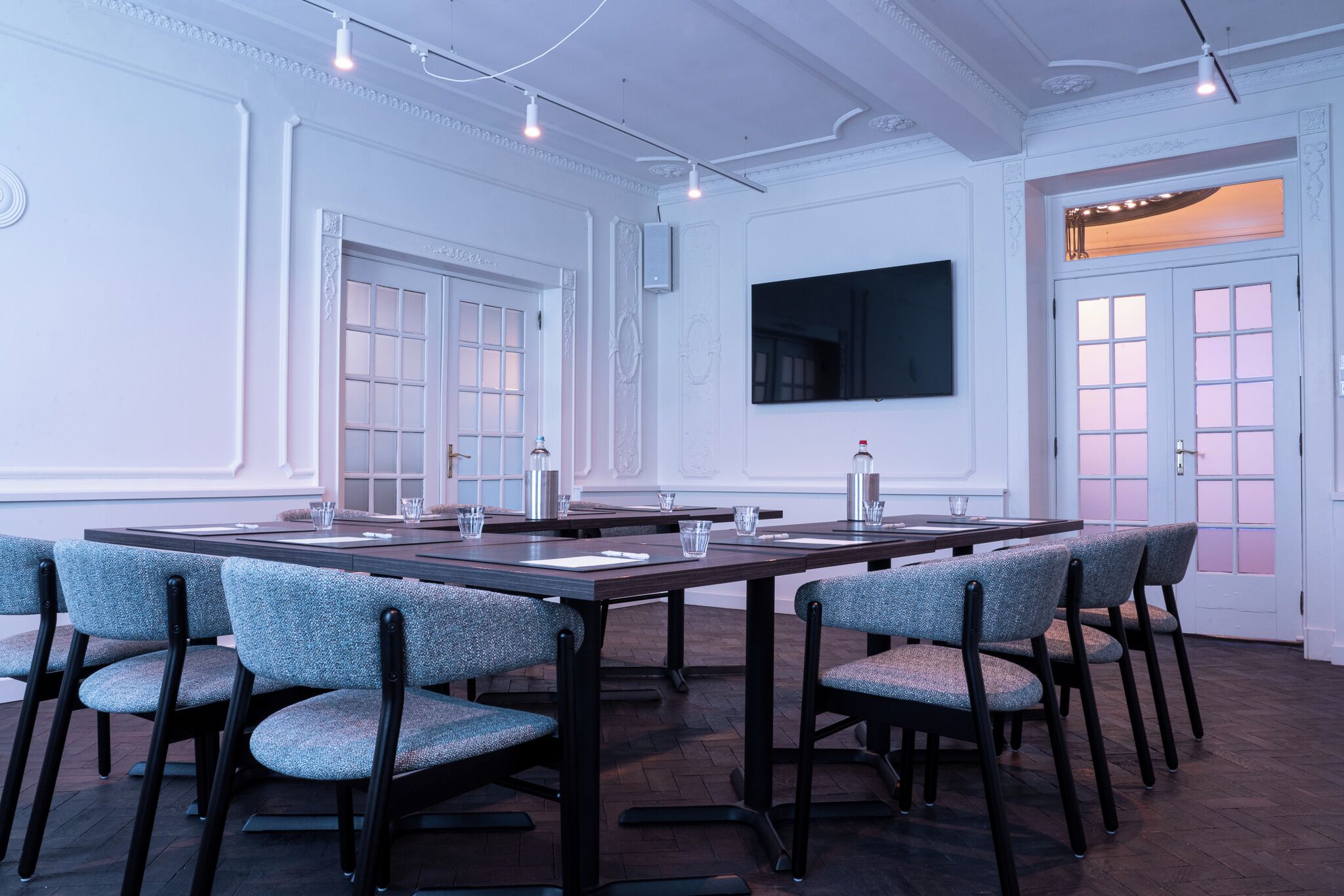 A conference room with a long table, chairs, a flat-screen TV, and a door with a window.
