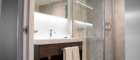 Un baño moderno con ducha de vidrio, un espejo grande y un perchero para toallas.