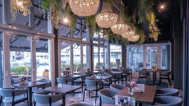 A restaurant with tables and chairs, large windows, and hanging lights. - Hampshire Hotel - Voncken Valkenburg (Valkenburg aan de Geul)