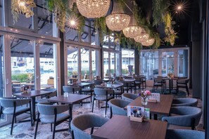 A restaurant with tables and chairs, large windows, and hanging lights. - Hampshire Hotel - Voncken Valkenburg (Valkenburg aan de Geul)